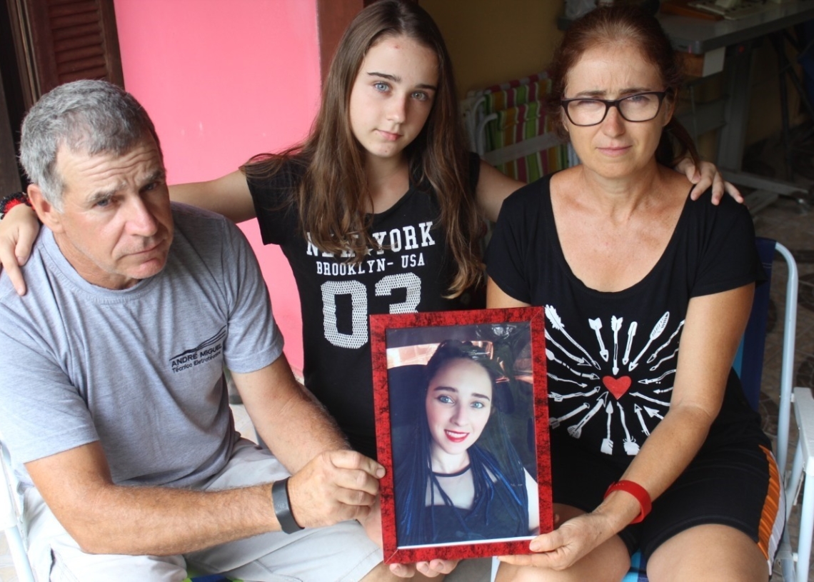 Os pais Paulo e Leopoldina e a irmã Gaziele seguram foto de Gabriele, assassinada em maio do ano passado em Araricá 
(Foto: Melissa Costa)